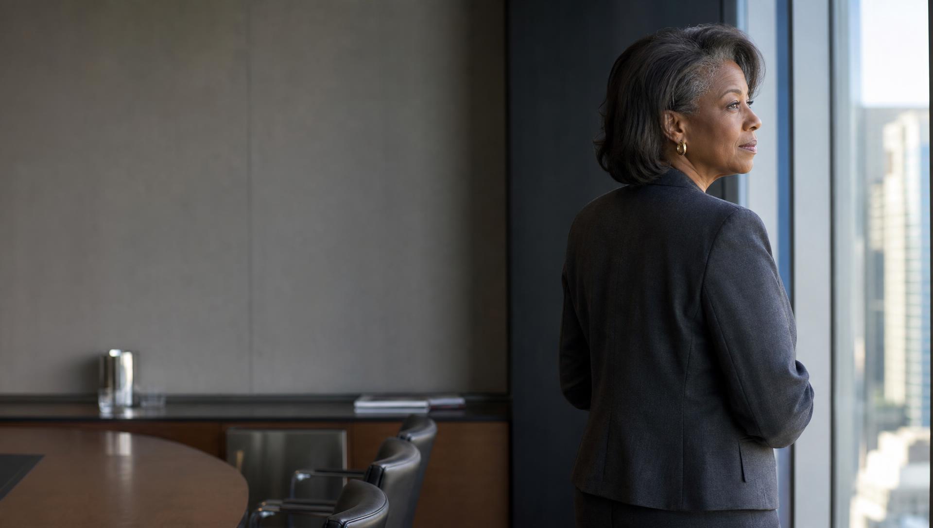 A senior executive standing at a boardroom window, city skyline beyond